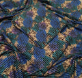 A close-up of draped fabric with a blue, teal, purple, and beige abstract pattern and fine vertical stripe texture.