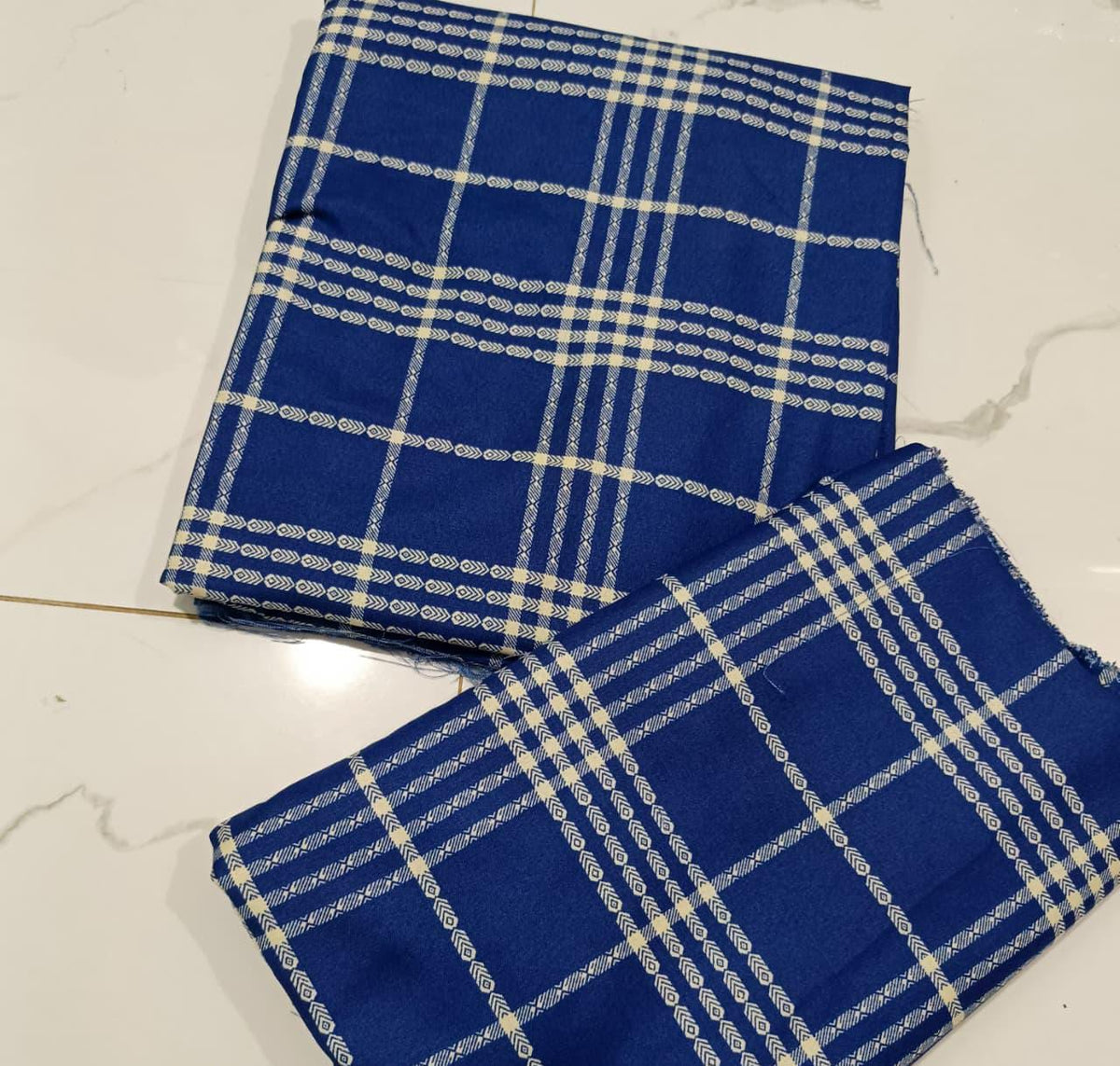 A folded piece of royal blue fabric with a white and light blue plaid pattern, displayed on a light marble surface.