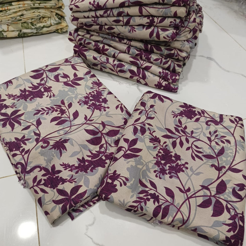 Folded fabric pieces with a floral vine pattern in deep purple and light gray on a warm beige background, arranged on a white tiled floor with more folded fabric stacked in the background.