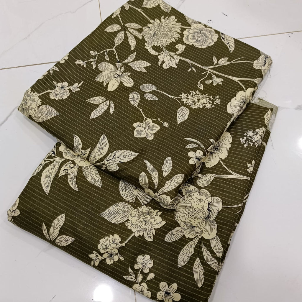 A folded piece of olive green fabric with a beige floral and leaf pattern, laid on a white tiled floor.